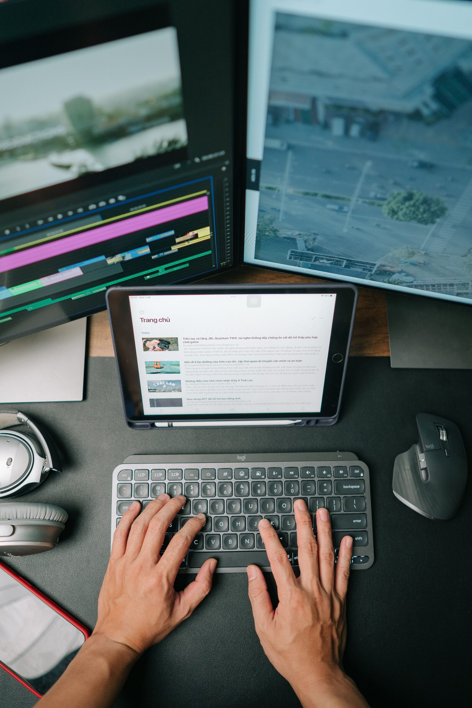 An overhead view of a multi-monitor editing desk, mid-edit, with a tablet and keyboard in reach.