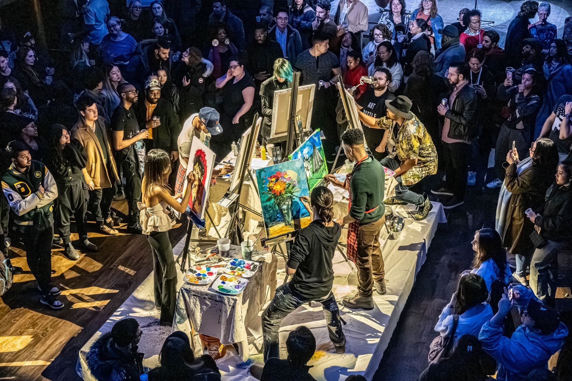 A crowd gathers around several painters working live at a community art event.