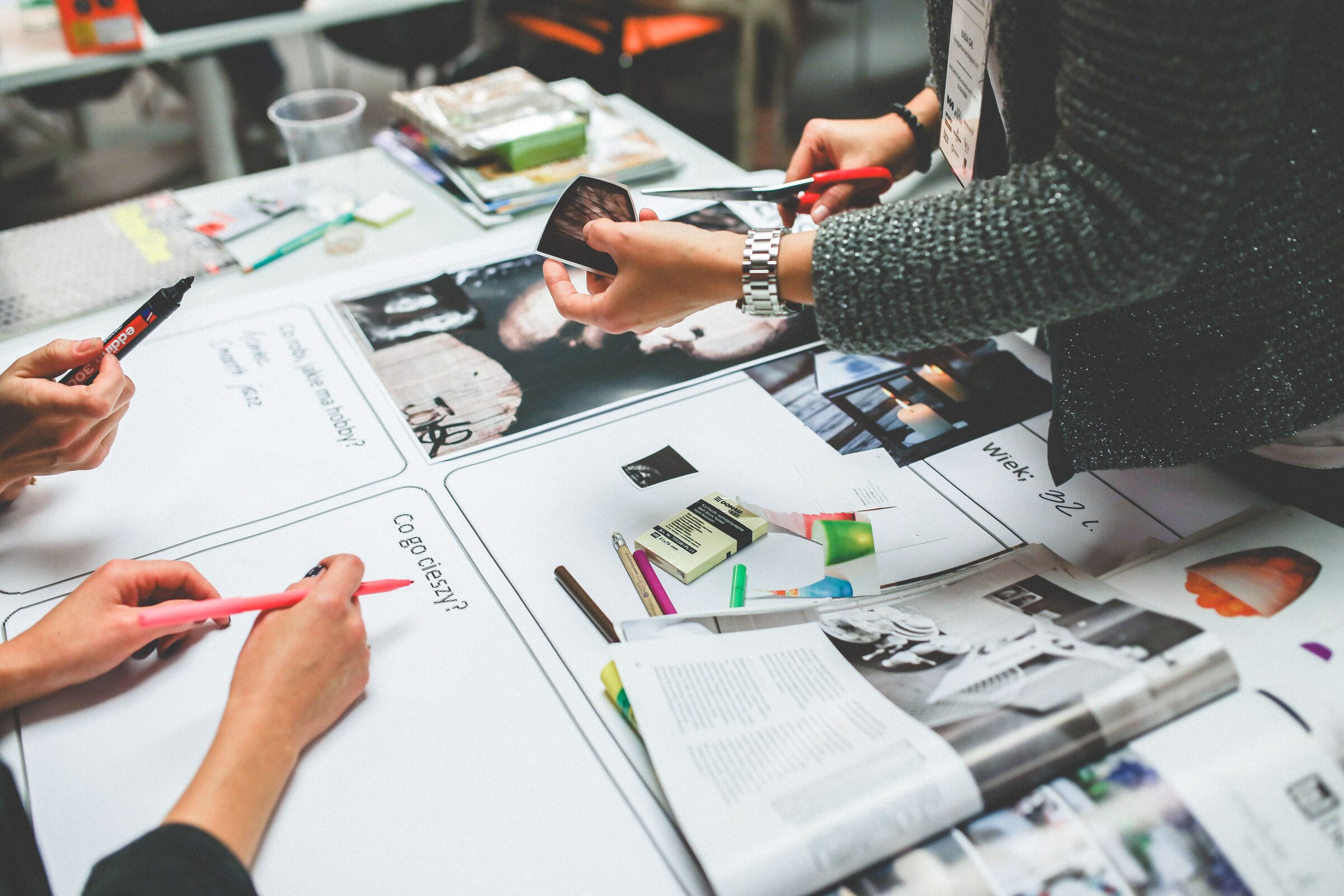 Several people collaborate around a table, cutting and arranging photographs onto a mood board.
