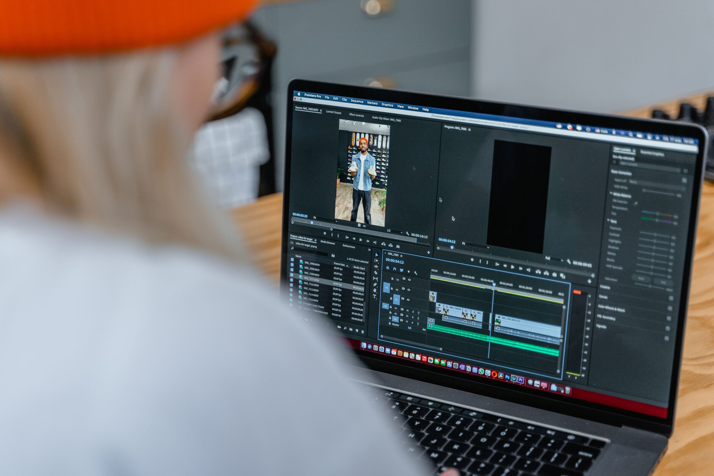 An editor works over their shoulder, cutting footage together in Premiere Pro.