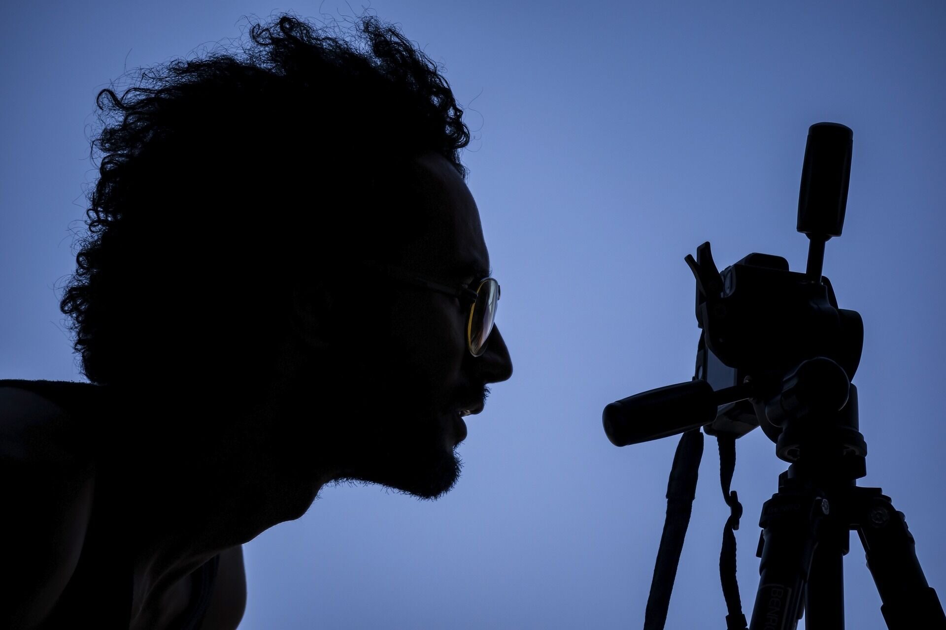 A photographer silhouetted against the dusk sky, framing a shot on a tripod-mounted camera.