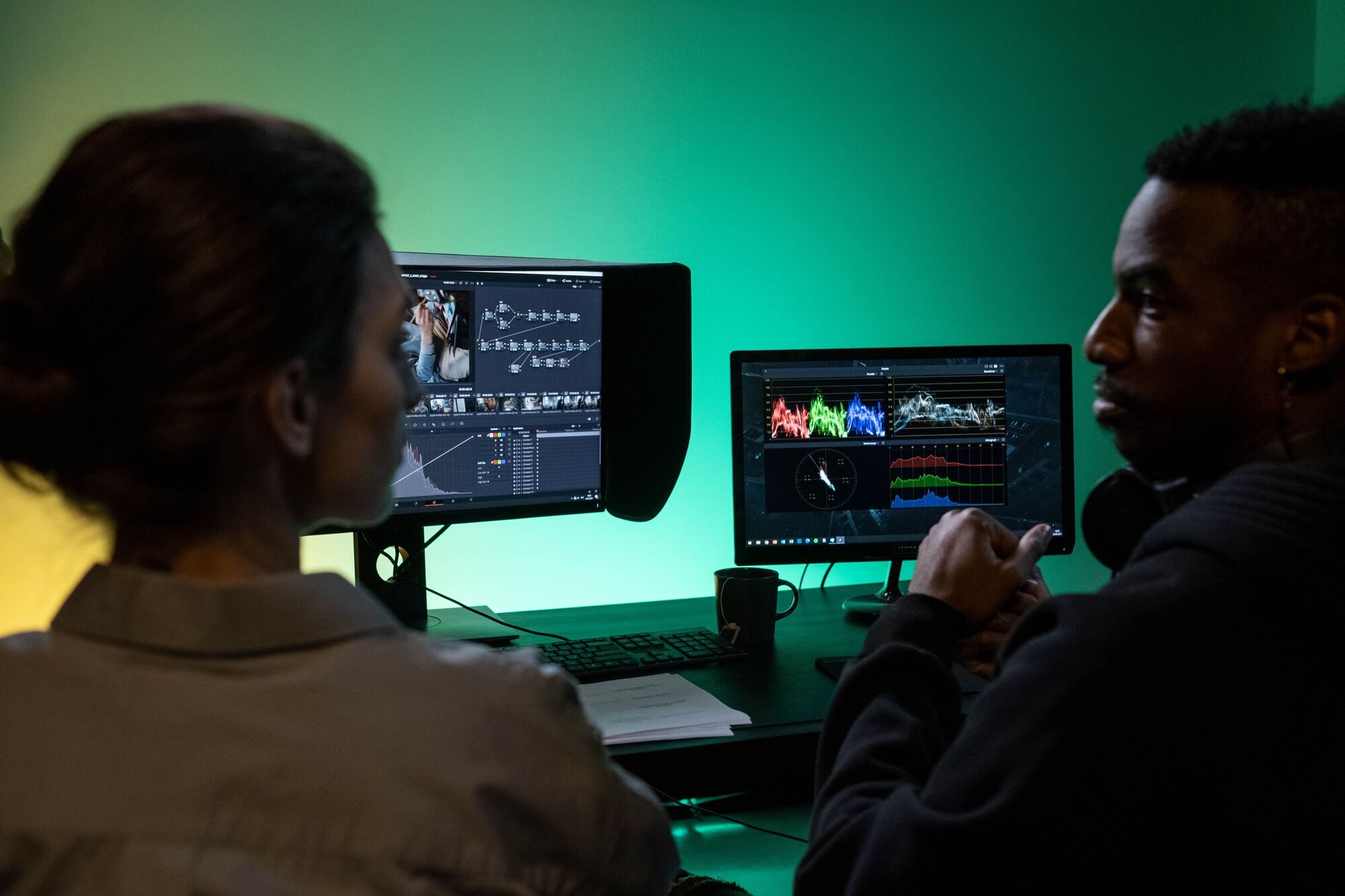 Two editors examine color-correction scopes together on a studio monitor.