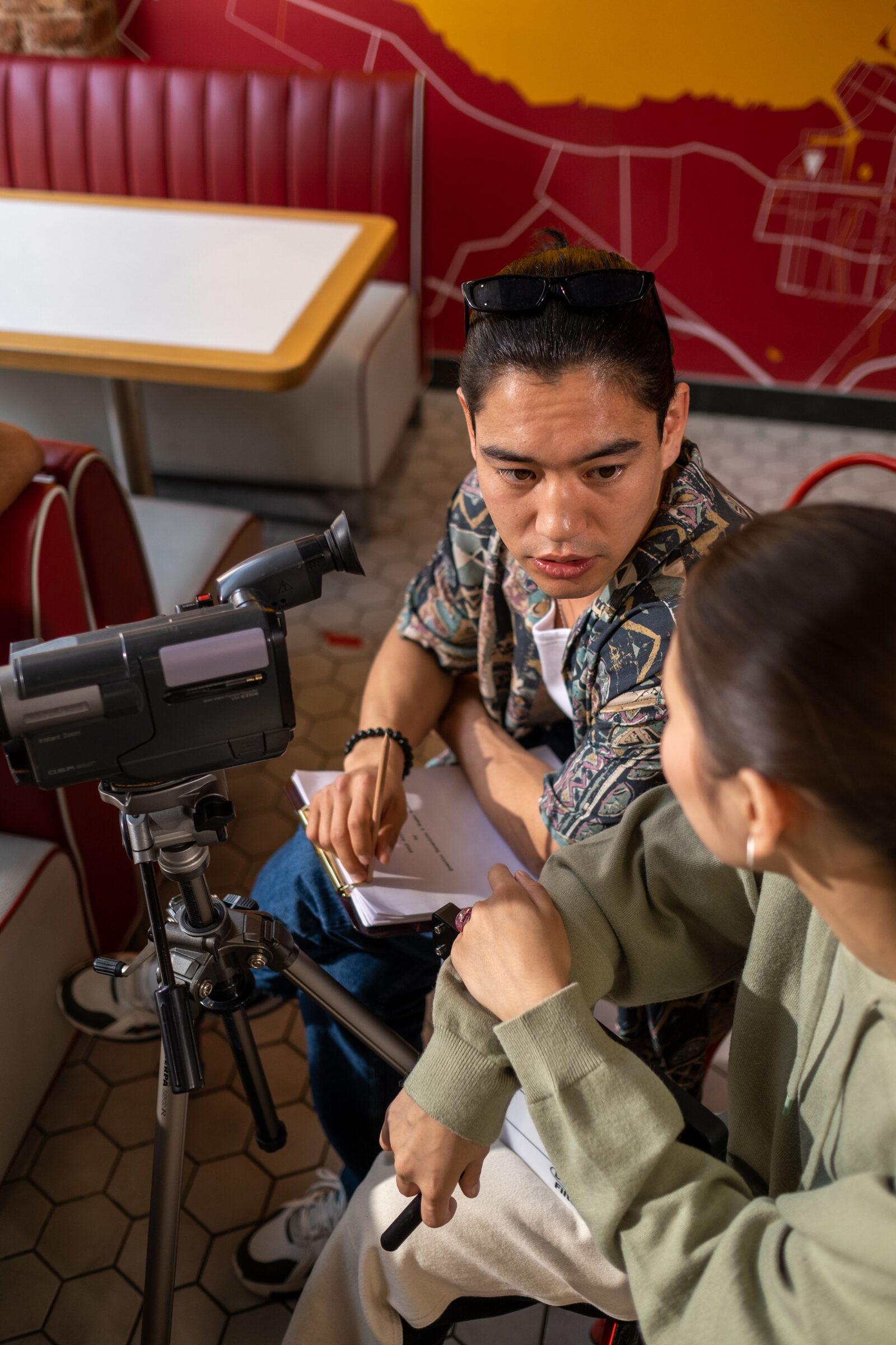 Two crew members review a script together beside a vintage camcorder on a tripod.